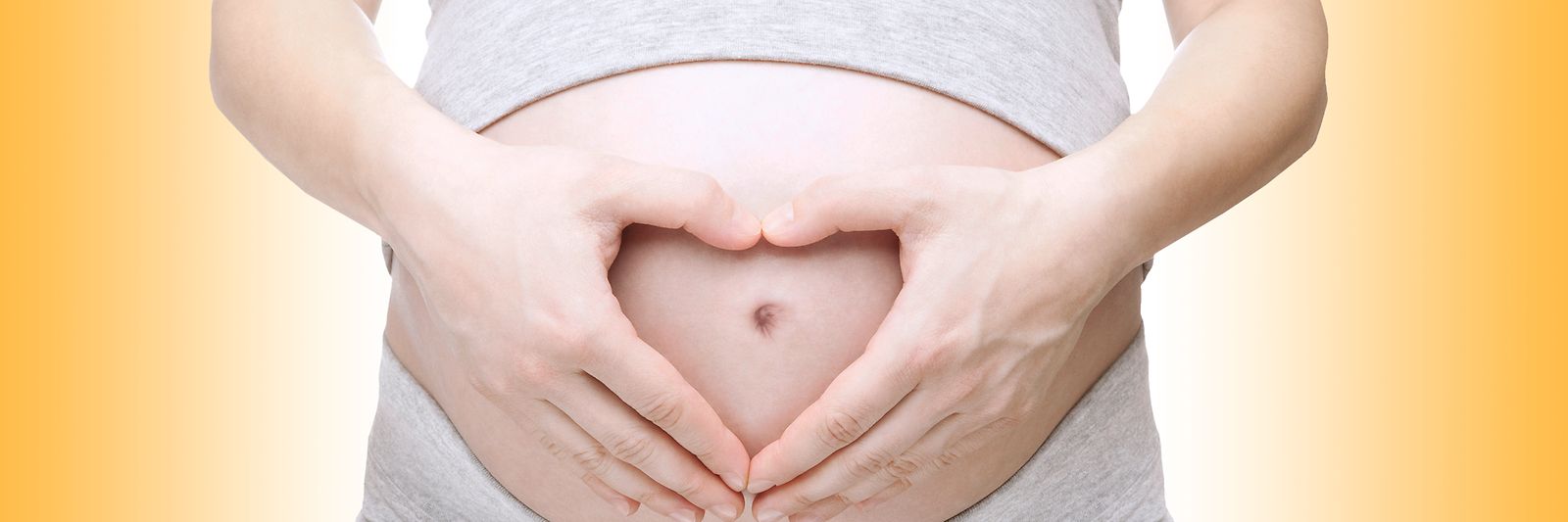 Hände formen ein Herz auf dem Bauch einer schwangeren Frau