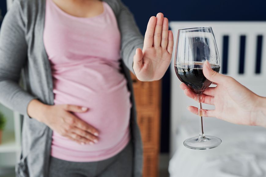 Schwangere Frau lehnt mit ausgestreckter Hand ein Glas Wein ab