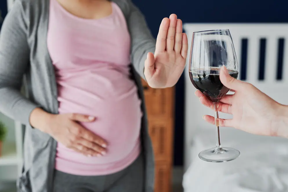 Schwangere Frau lehnt mit ausgestreckter Hand ein Glas Wein ab