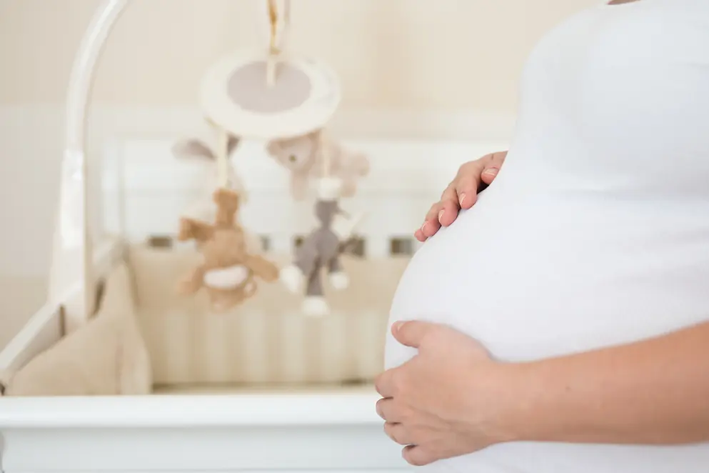 Eine schwangere Frau hält Ihren Bauch vor einem Kinderbett